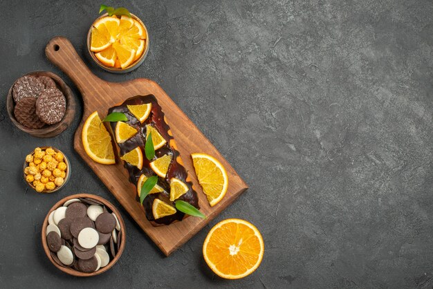 Vista anterior de sabrosos pasteles cortan naranjas con galletas en la tabla de cortar en la mesa oscura