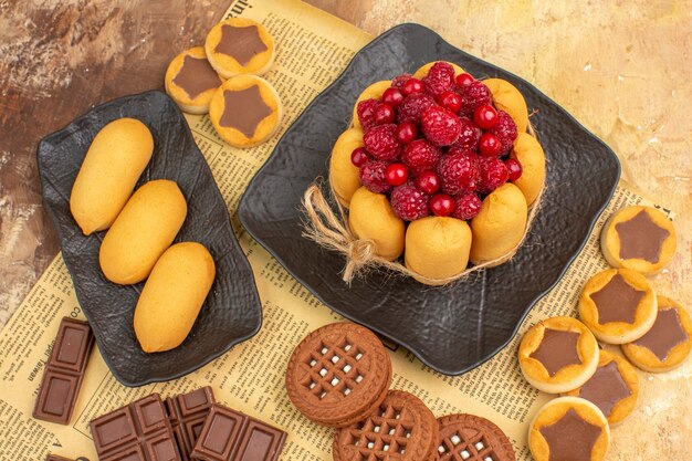 Vista anterior de sabrosos pasteles diferentes galletas en placa marrón sobre tabla de colores mezclados