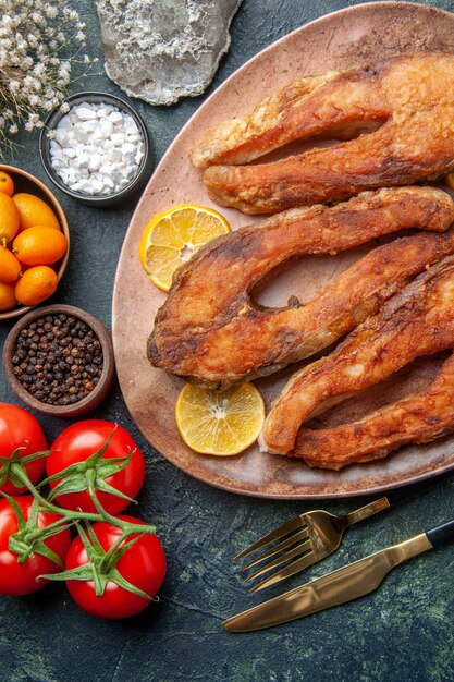 Vista anterior de sabrosos pescados fritos y rodajas de limón en una placa marrón tomates kumquats en mesa de mezcla de colores con espacio libre