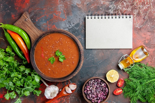 Vista anterior de sopa de tomate frijoles botella de aceite caído en la tabla de cortar y el portátil en una tabla de colores mezclados