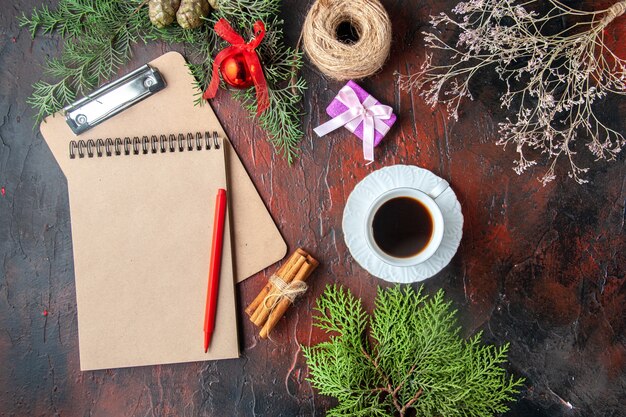 Vista anterior de una taza de té negro ramas de abeto canela limas regalo y cuaderno sobre fondo oscuro