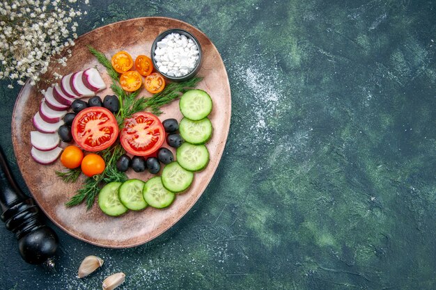 Vista anterior de verduras frescas picadas, aceitunas, sal en una placa marrón y un martillo de cocina en el lado derecho de la tabla de colores mezclados verde negro