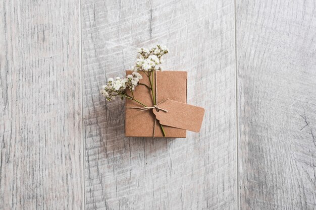 Una vista desde arriba de la caja de cartón atada con etiquetas y flores de aliento de bebé en el escritorio de madera