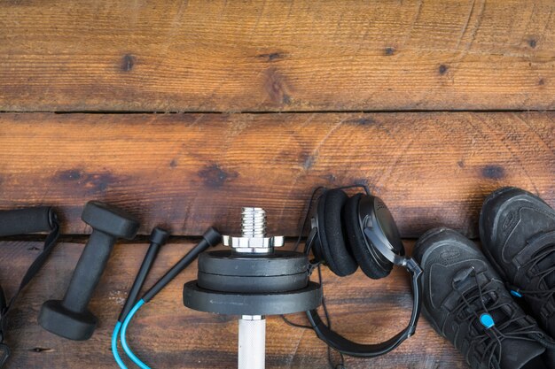Una vista desde arriba de la correa de fitness; mancuernas Cuerda saltar; pesos auriculares y zapatos en madera con textura de fondo
