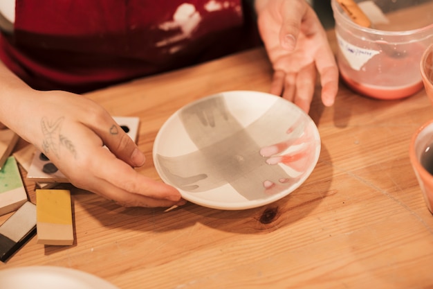 Una vista desde arriba del decorador de cerámica femenino que sostiene una placa de cerámica pintada