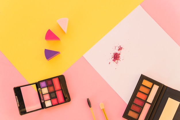 Foto gratuita una vista desde arriba de las herramientas de maquillaje profesional y la paleta de sombras de ojos en colores de fondo