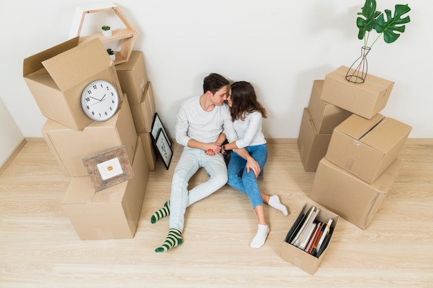 Una vista desde arriba de la joven pareja besándose sentados con cajas de cartón en su nuevo hogar