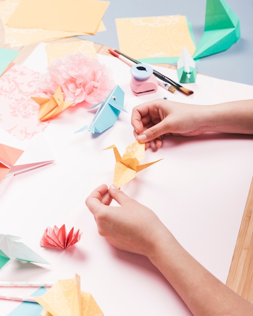 Vista de arriba de la mano humana que sostiene el pájaro de origami sobre la mesa