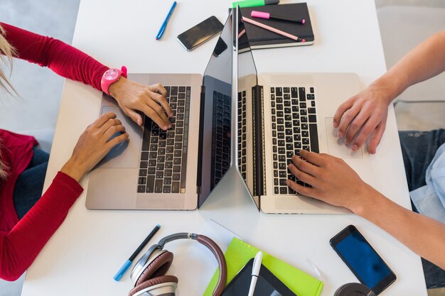 Vista desde arriba de las manos del joven y la mujer que trabaja en la computadora portátil en la oficina de trabajo conjunto, escribiendo en el teclado