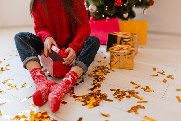 Vista desde arriba de la mujer en calcetines rojos sentada en su casa en navidad en confeti dorado desempacando peresents y cajas de regalo