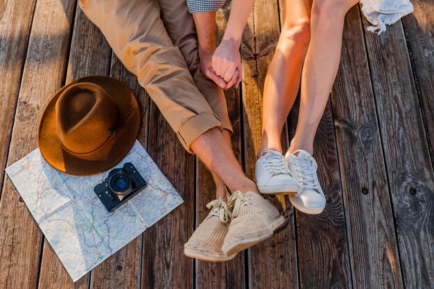 Vista desde arriba de las piernas de una pareja que viaja en verano vestida con zapatillas de deporte, moda de estilo hipster boho hombre y mujer divirtiéndose juntos, mapa, sombrero, cámara de fotos, turismo, moda de calzado