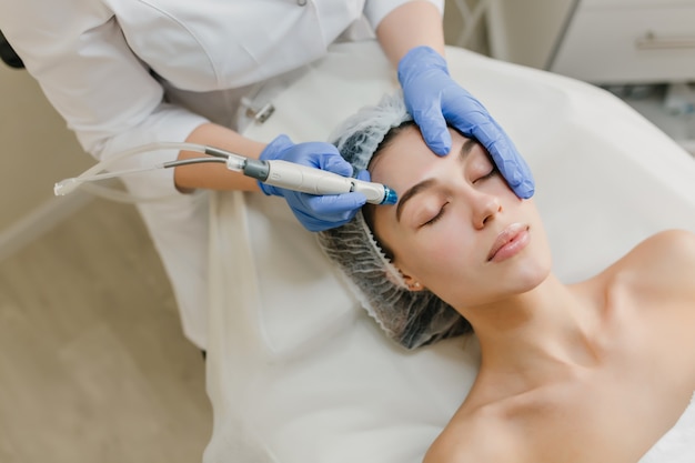 Vista desde arriba del rejuvenecimiento de hermosa mujer disfrutando de procedimientos de cosmetología en salón de belleza. Dermatología, manos en resplandores azules, salud, terapia, botox