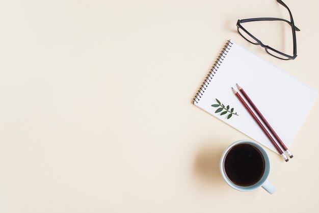 Una vista desde arriba de la taza de té; Anteojos y lápiz en libreta espiral sobre fondo beige