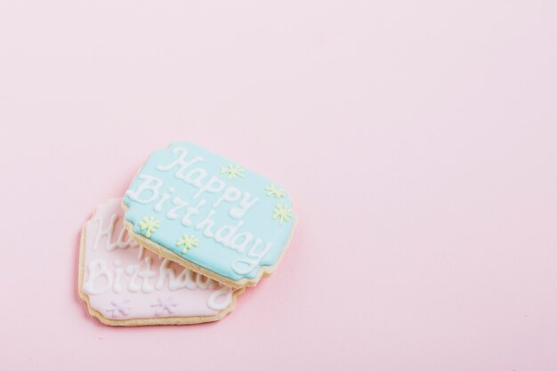 Vista de arriba del texto del feliz cumpleaños en las galletas frescas sobre fondo rosado