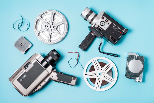 Una vista desde arriba de las tiras de película; Rollo de película y varios tipos de videocámaras sobre fondo azul