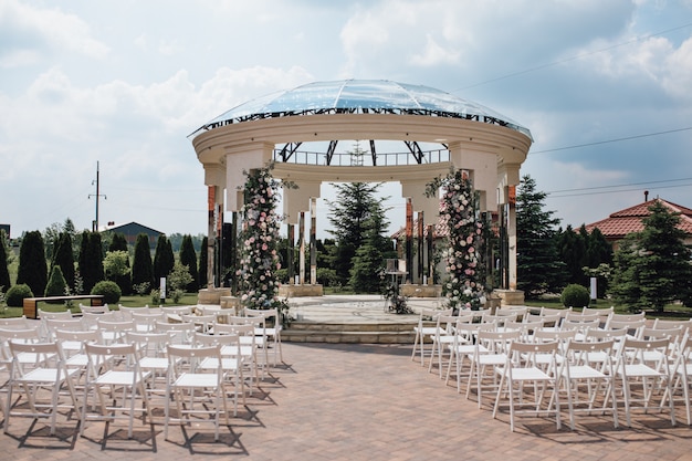 Vista de los asientos para invitados y el arco de bodas ceremoniales en el soleado por ejemplo, sillas chiavari, territorio decorado