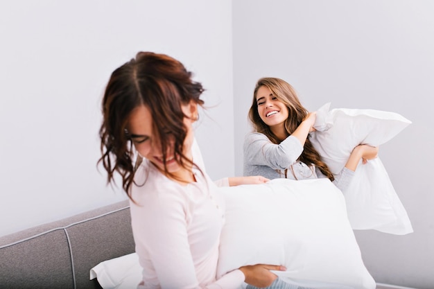 Foto gratuita vista desde atrás chica recibiendo un golpe de chica con almohada. usan pijamas y se divierten en la cama.