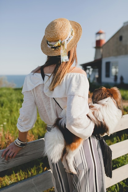 Vista desde atrás de la mujer elegante en el campo, sosteniendo un perro