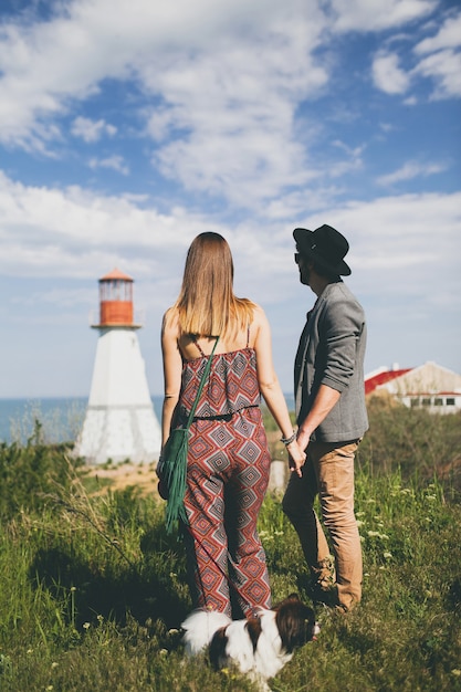 Vista desde atrás en pareja joven inconformista elegante enamorado caminando con perro en campo