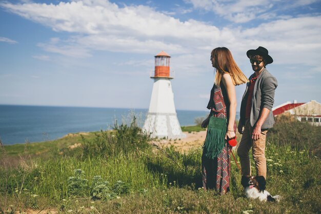 Vista desde atrás en pareja joven inconformista elegante enamorado caminando con perro en campo