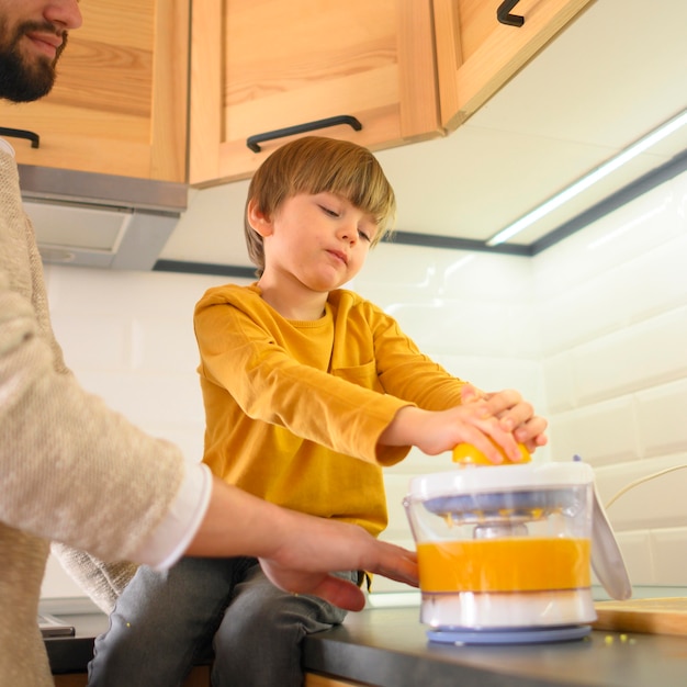 Vista baja niño y papá haciendo jugo de naranja