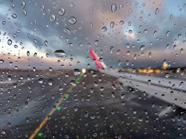 Vista borrosa de la pista de un aeropuerto a través de la ventana de un avión con gotas de lluvia