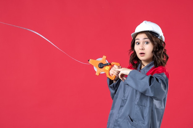 Vista de cerca de la arquitecta preocupada en uniforme con cinta métrica de apertura de casco en pared roja aislada