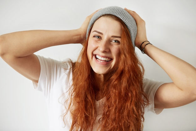 Vista de cerca de la atractiva joven con largo cabello rojo suelto, vestida con camiseta blanca y gorra gris