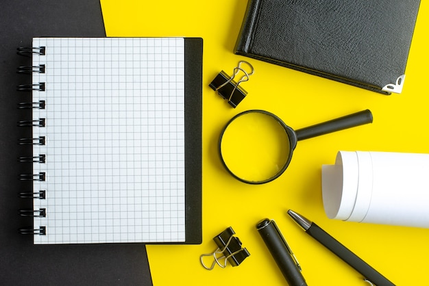 Vista de cerca de los bolígrafos de lupa de los espacios en blanco del cuaderno espiral sobre fondo de colores de mezcla amarillo negro