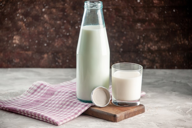 Vista de cerca de la botella de vidrio abierta y la taza llena de leche en una toalla pelada púrpura sobre una tabla de cortar de madera