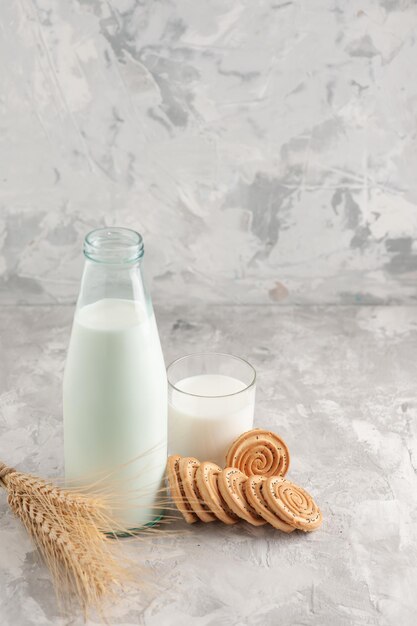 Vista de cerca de la botella de vidrio y la taza llena de leche y galletas pico en la superficie blanca manchada