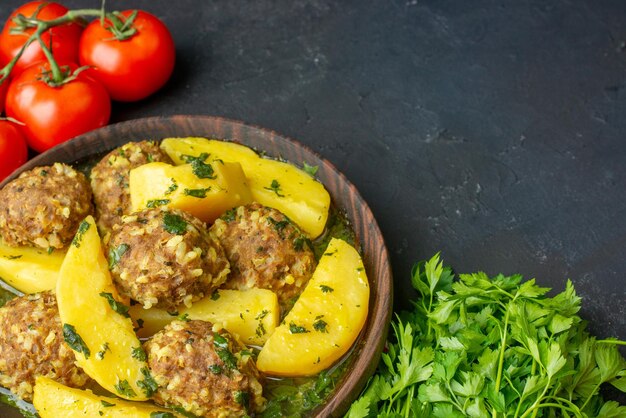 Vista de cerca de una cena sabrosa con albóndigas, papas verdes en un tazón marrón sobre tomates de toalla pelados rojos sobre fondo negro con espacio libre