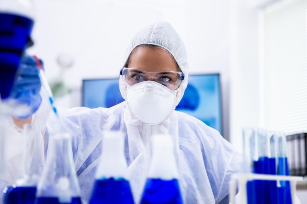 Vista de cerca del científico tomando una muestra de solución azul con una pipeta de un tubo de ensayo.
