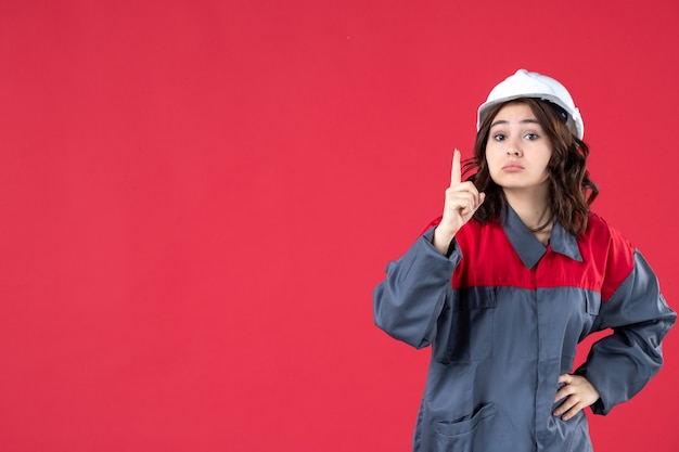 Vista de cerca de la constructora sorprendida en uniforme con casco y apuntando hacia arriba en la pared roja aislada