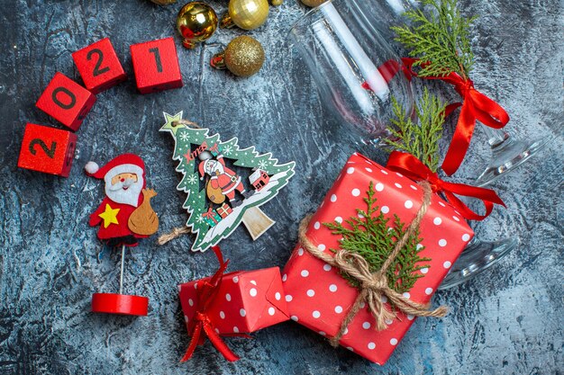 Vista de cerca de las copas de vidrio caídas y cubiertos, accesorios de decoración, caja de regalo y números de calcetines navideños en la mesa oscura