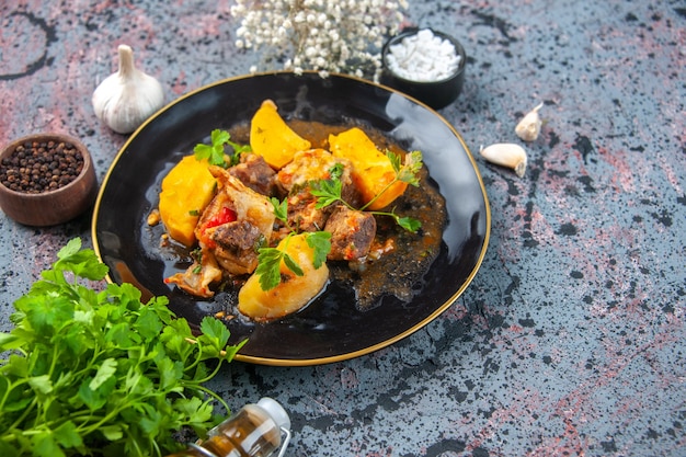 Vista de cerca de la deliciosa cena con patatas de carne servidas con verde en un plato negro y especias de ajo flor de botella de aceite caído sobre fondo de colores de mezcla