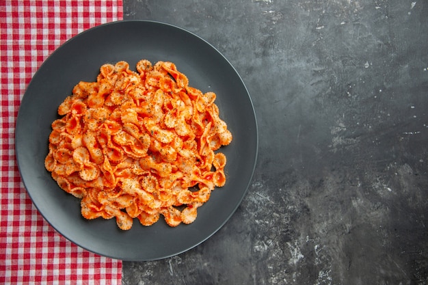 Vista de cerca de la deliciosa comida de pasta en un plato negro para cenar sobre una toalla despojada de rojo sobre fondo oscuro