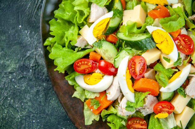 Vista de cerca de deliciosa ensalada casera en una placa negra en el lado izquierdo sobre fondo verde negro mezcla de colores con espacio libre