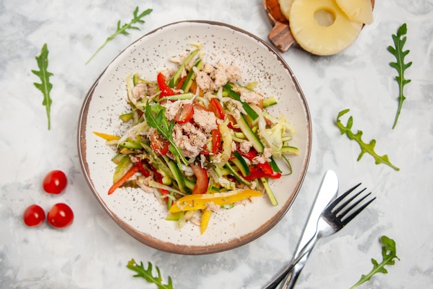 Vista de cerca de la deliciosa ensalada de pollo con verduras, tomates, piñas secas, cubiertos en superficie blanca manchada