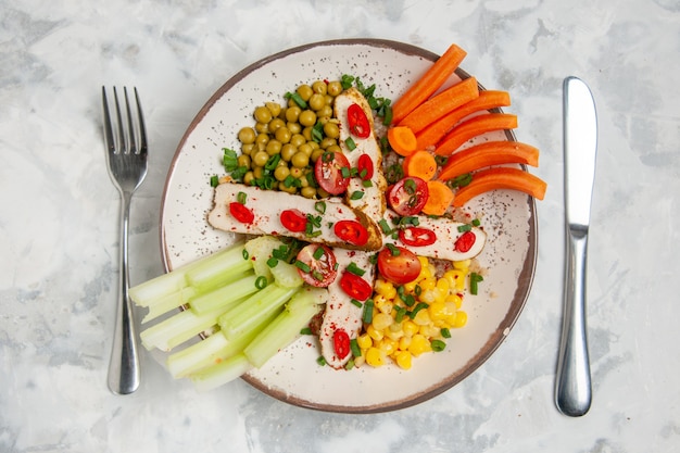 Vista de cerca de una deliciosa ensalada con varios ingredientes en un plato y cubiertos en una superficie blanca con espacio libre