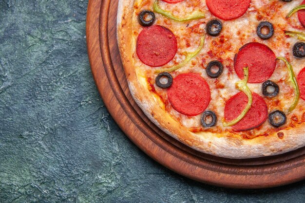 Vista de cerca de una deliciosa pizza en una tabla de cortar de madera en el lado izquierdo sobre una superficie azul oscuro con espacio libre
