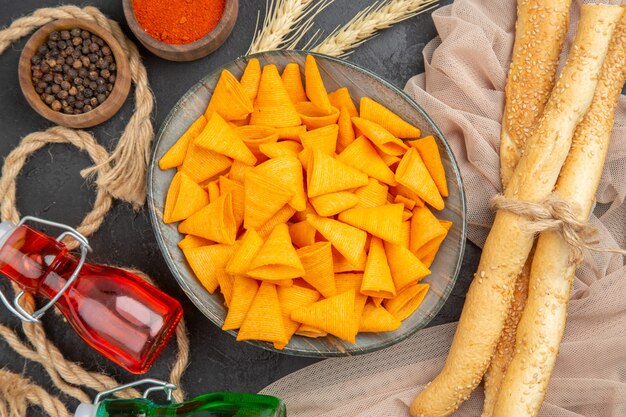 Vista de cerca de deliciosas patatas fritas caídas botellas pimientos sobre una toalla y cuerda sobre un fondo negro