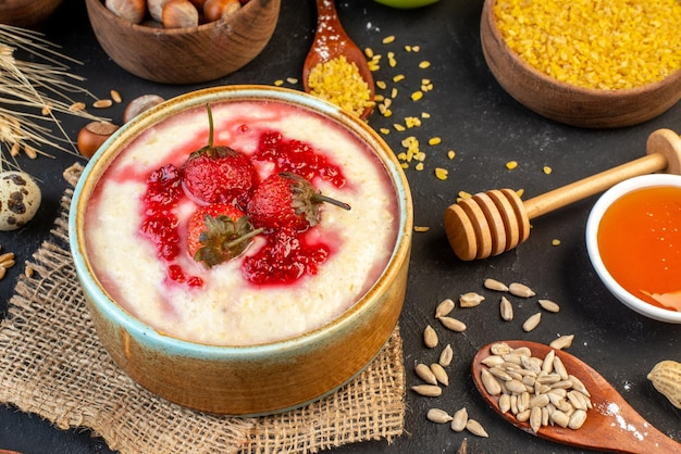 Vista de cerca del delicioso desayuno servido con mermelada de fresas en un tazón y huevos de avellanas arroz amarillo sobre fondo de color oscuro