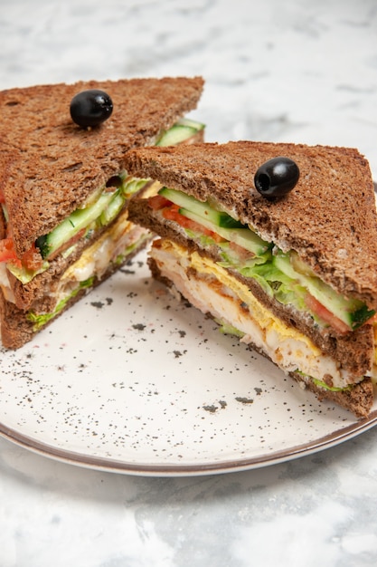 Vista de cerca del delicioso sándwich con pan negro decorado con oliva en un plato sobre la superficie blanca manchada