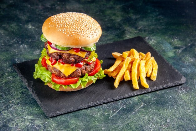 Vista de cerca de delicioso sándwich y papas fritas en bandeja de color oscuro sobre superficie negra