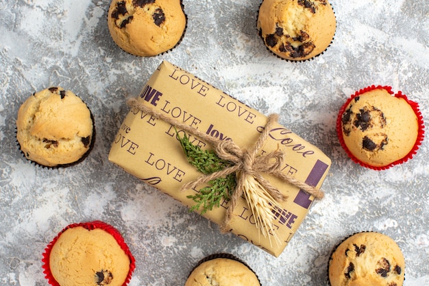 Vista de cerca de deliciosos cupcakes pequeños con chocolate alrededor de regalo con inscripción de amor en la superficie del hielo