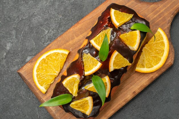 Vista de cerca de deliciosos pasteles decorados con naranja y chocolate en la tabla de cortar en el cuadro negro