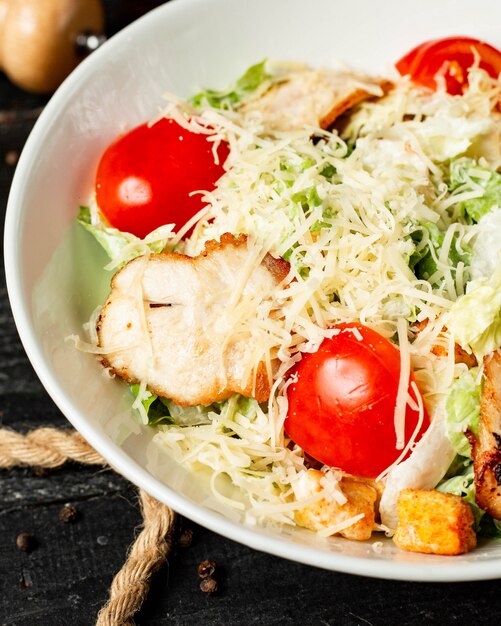 Vista de cerca de ensalada César con tomate pollo y queso parmesano en un tazón