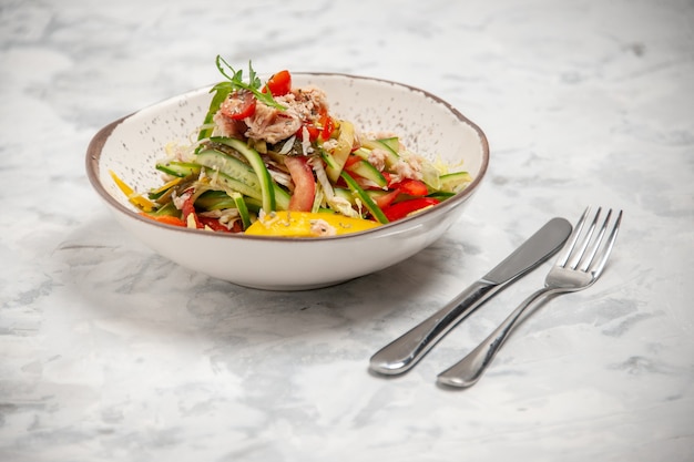 Vista de cerca de ensalada de pollo con verduras y cubiertos en superficie blanca manchada