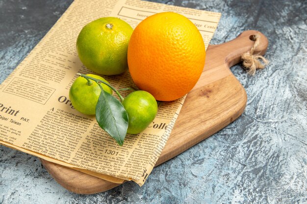 Vista de cerca de frutas cítricas frescas con hojas y periódico en la tabla de cortar de madera cortada en la mitad de la tabla gris de formas